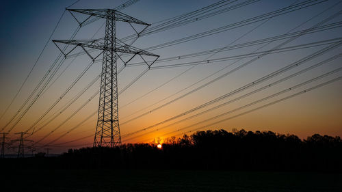 Low angle view of silhouette electricity pylon against sky during sunset