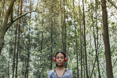 Young woman with eyes closed listening music through headphones against trees at park