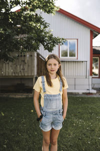 Pre-adolescent girl with hands in pockets standing in back yard