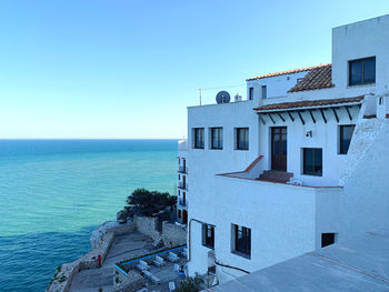 Lighthouse by sea against clear blue sky