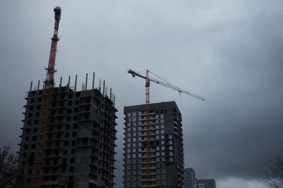 Low angle view of crane by building against sky