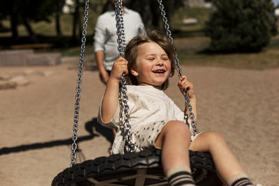 Smiling girl sitting on tire swing and swinging