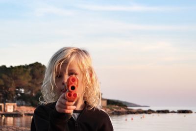 Portrait of cute boy holding squirt gun against sea and sky during sunset