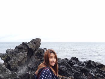 Portrait of young woman on rock by sea against sky