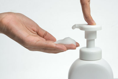 Close-up of hand holding bottle against white background