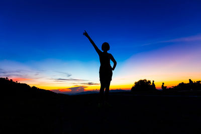 Silhouette woman standing on field against sky during sunset