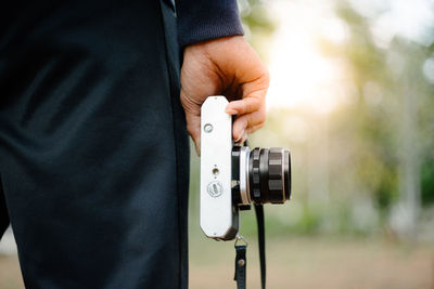 Midsection of man holding camera while standing outdoors