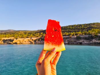 Midsection of person holding ice cream against sky