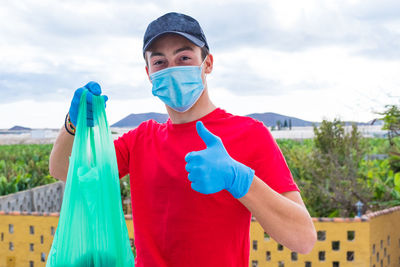 Portrait of teenager boy wearing mask holding garbage standing outdoors