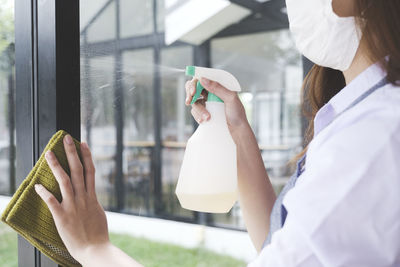 Midsection of woman cleaning glass window with spray