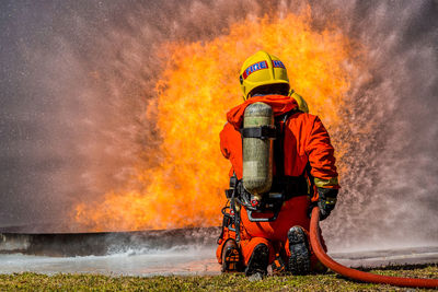 Rear view of firefighter spraying water on field