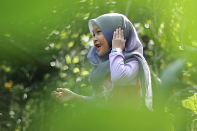 Smiling girl wearing hijab amidst plants