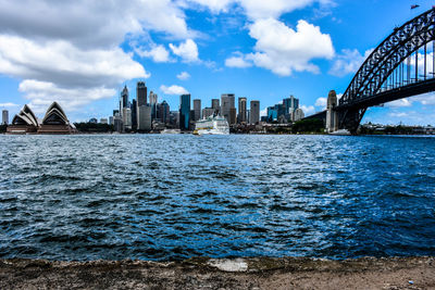 View of city at waterfront against cloudy sky