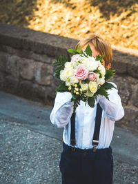 Cute boy holding bouquet standing outdoors