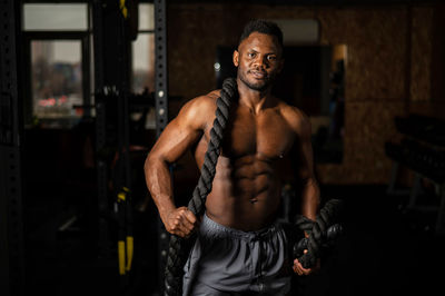 Muscular african american man posing with rope in gym. 