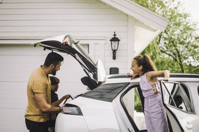 Smiling girl talking to father loading stuff in car trunk