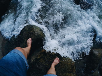 Low section of person standing on rock by sea