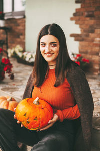 A beautiful girl with dark hair with makeup for the celebration of halloween holds a pumpkin 