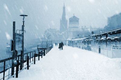 Rear view of people walking on snow covered street in city during winter