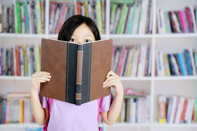 Portrait of girl holding book at library