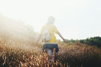 Rear view of woman walking on field against sky