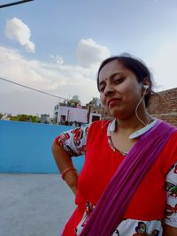 Young woman looking away while standing against sky