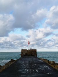 Lighthouse on pier over sea against sky