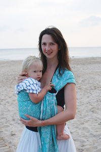 Portrait of young woman holding baby standing at beach