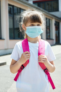 Portrait of a girl with a backpack in a medical mask at the schoolyard. protection of children 