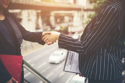 Midsection of businesswomen handshaking on steps with street in background