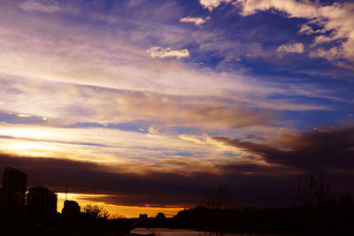 Silhouette of city against cloudy sky during sunset