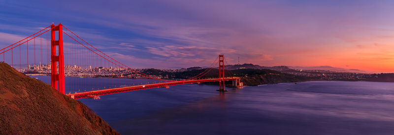 Suspension bridge over river against sky during sunset