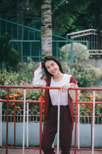 Portrait of smiling young woman standing against railing