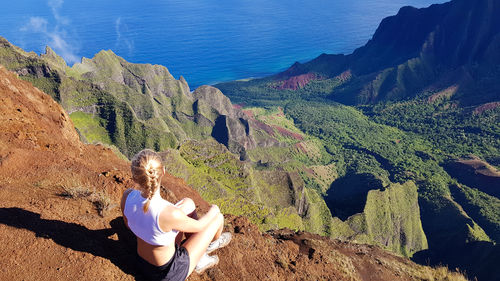 Rear view of woman sitting on cliff during sunny day