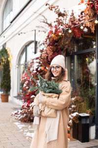 A stylish young woman wearing a hat with branches of nobilis in a craft bag walks  the christmas