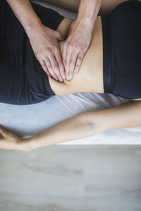 Professional female therapist pressing hands on belly of patient during lymphatic drainage treatment in modern rehabilitation clinic