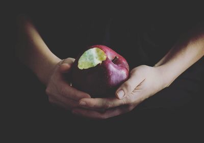 Close-up of hand holding apple against black background