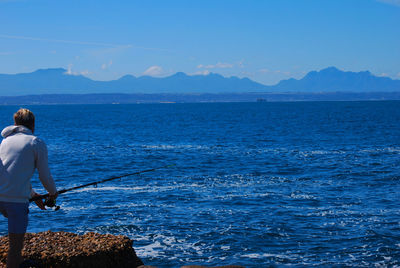 Rear view of man fishing in sea against sky