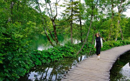 Portrait of woman standing footbridge over lake against plants