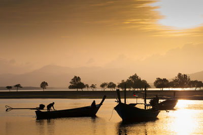 Silhouette people in boat on lake during sunset