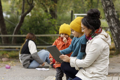 Woman with children at playground using digital tablet