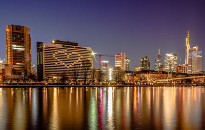 Illuminated buildings by river against sky at night