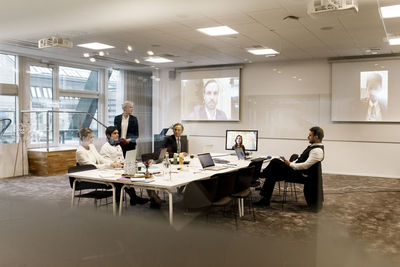 Mature businesswoman planning strategy with team in board room during web conference meeting at office