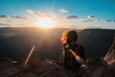 Rear view of woman sitting against sky during sunset