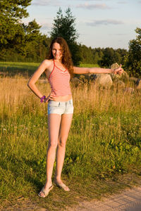 Full length portrait of smiling woman gesturing thumbs up while hitchhiking on land