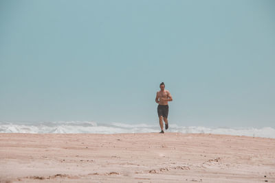 Rear view of shirtless man standing on beach against sky