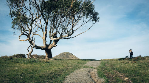 Photographer by pathway on grassy field against sky