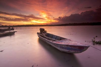 Boat moored on sea against sky during sunset