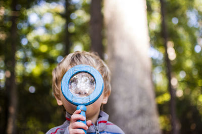 Boy looking through magnifying glass in forest