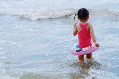 Rear view of girl with inflatable ring wading in sea